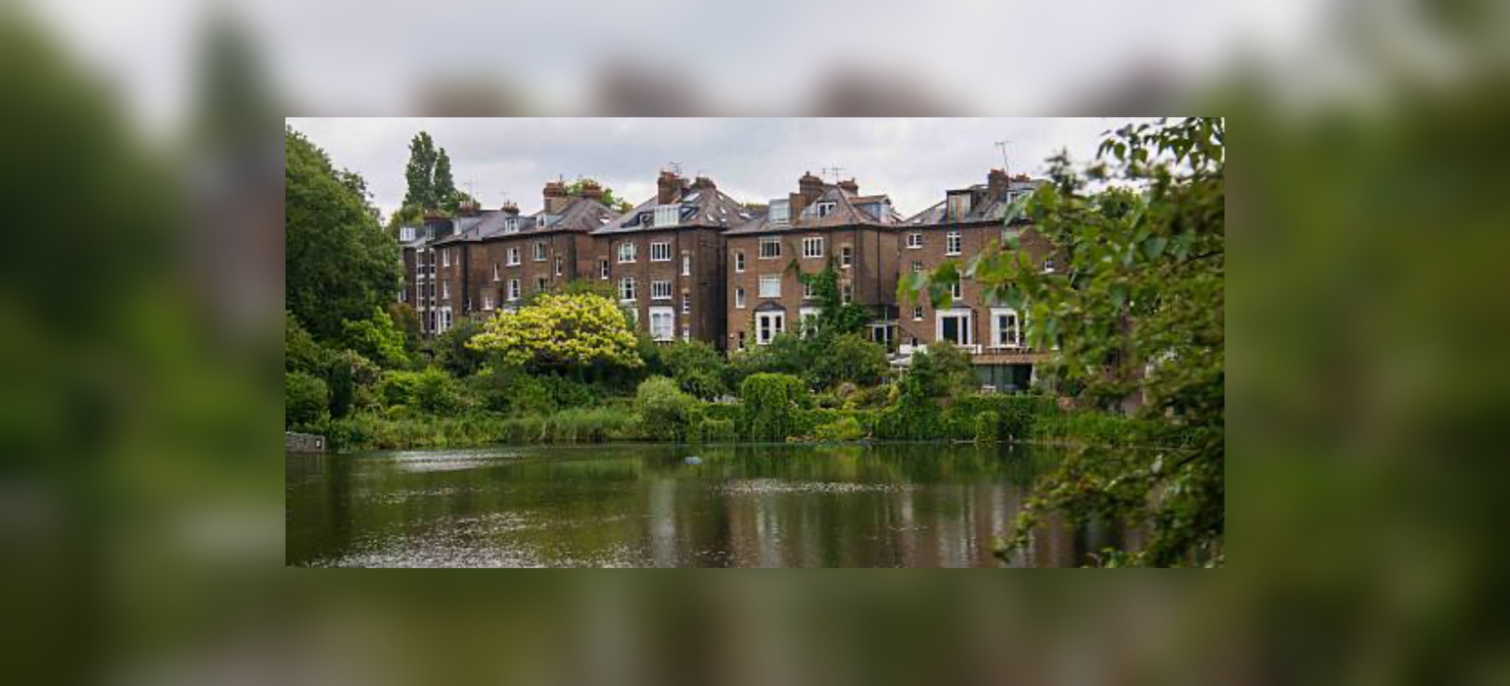 Residential properties overlooking a pond, seen across a wide green landscape