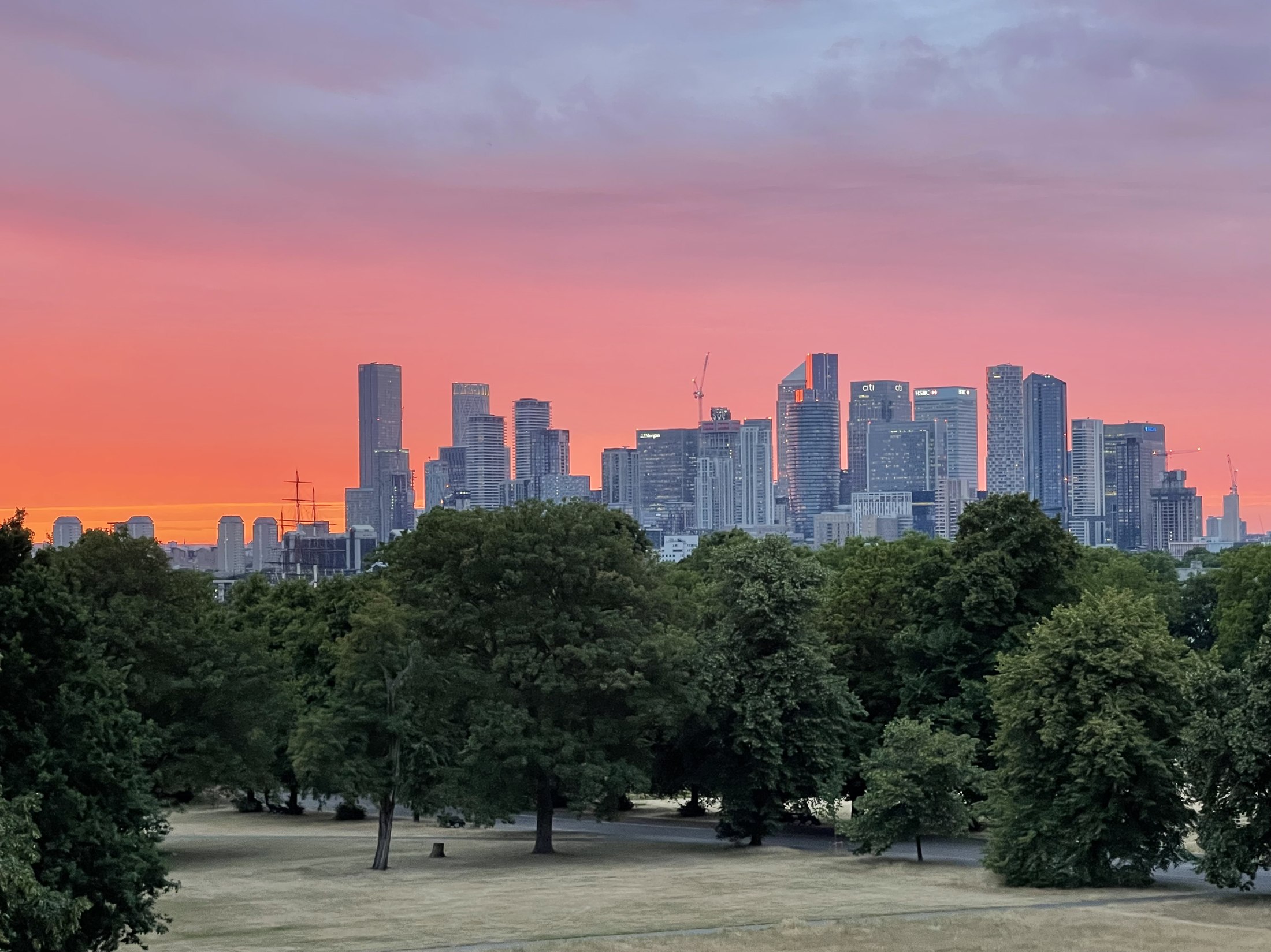 London skyline at sunset, seen across a park with the city's towers in the distance